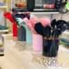 Colorful silicone kitchen utensil sets with wooden handles neatly arranged in matching holders on a white countertop in a modern kitchen display